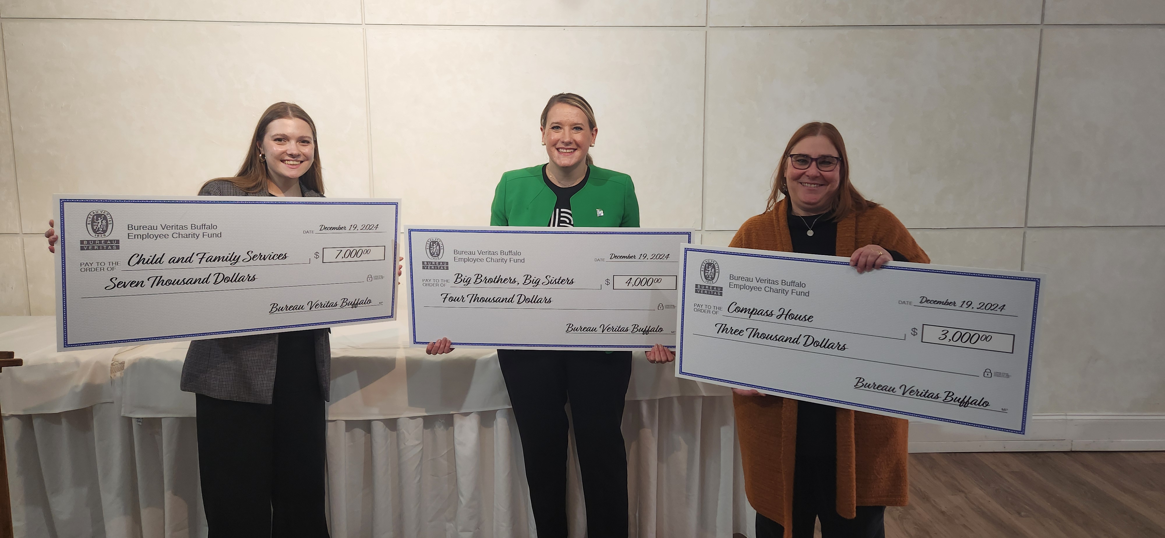 3 women from Child and Family Services, Compass House, and Big Brothers Big Sisters holding large checks with donations from the Bureau Veritas Buffalo team